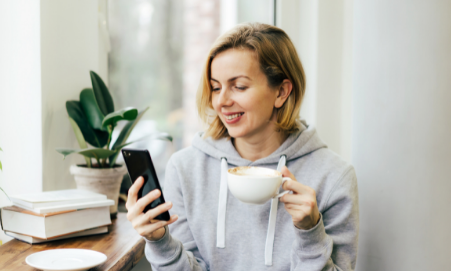 Woman in Sweatshirt with coffee cup and looking at phone